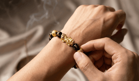 Close-up of a man correctly placing a Pixiu bracelet on his left wrist with the head facing outward.